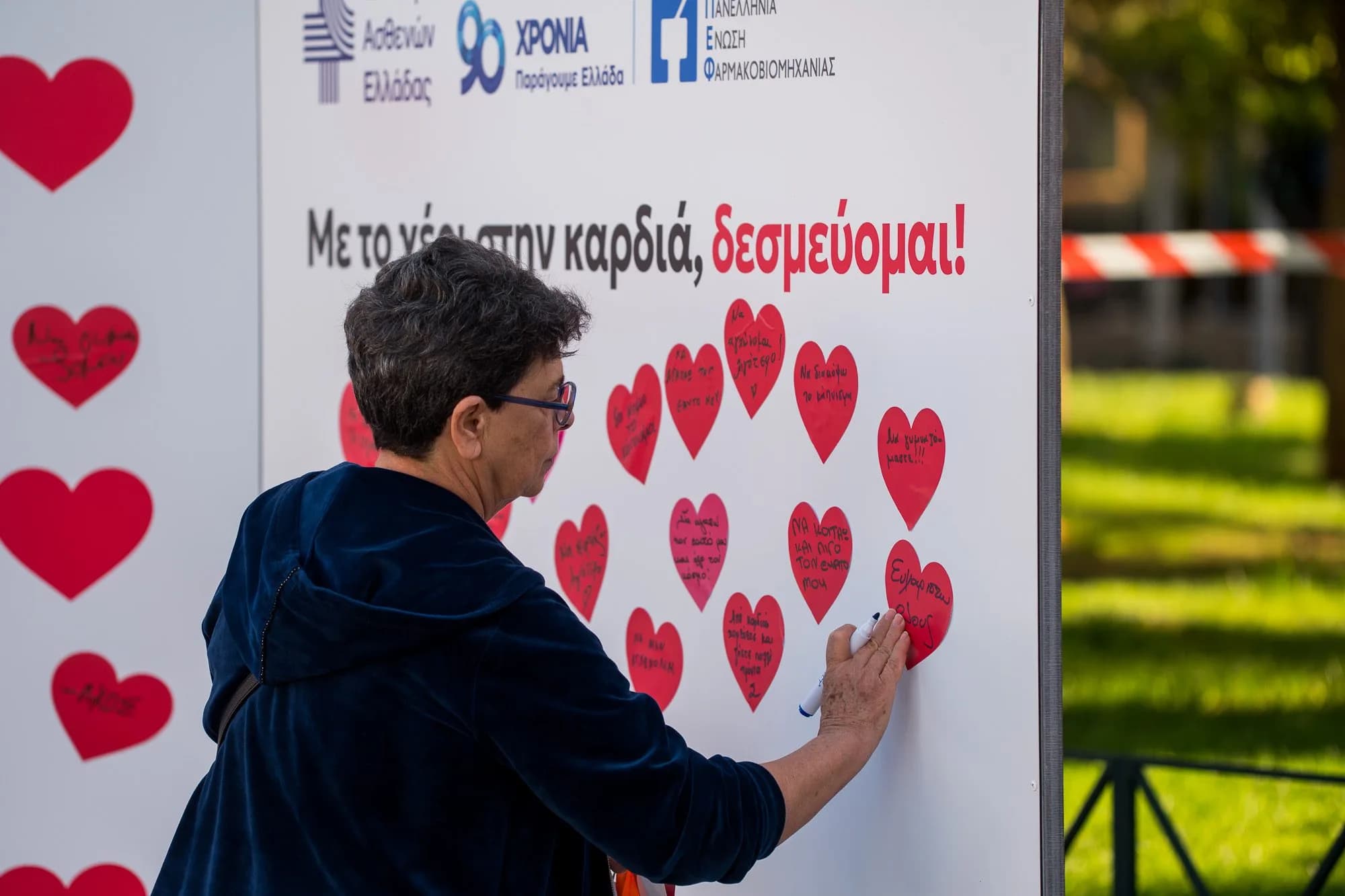 Επισκέπτρια κολλά τη χάρτινη καρδιά της στον τοίχο των δεσμεύσεων.